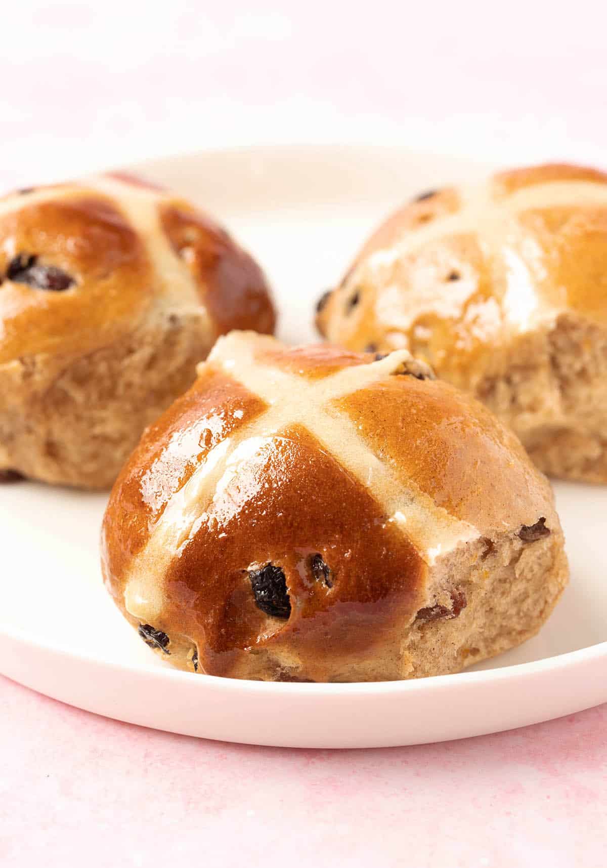 A plate of homemade Hot Cross Buns on a pink backdrop.
