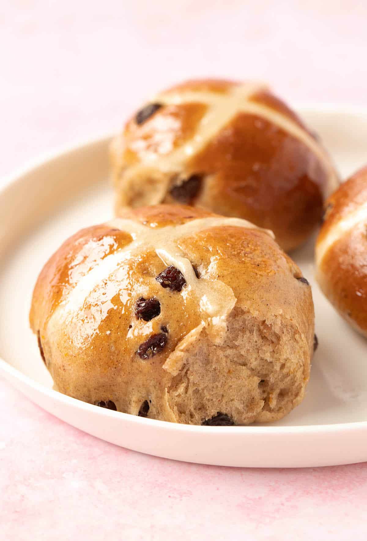 Hot cross buns sitting on a white plate. 