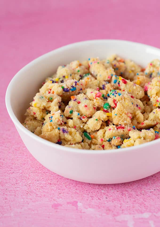 A bowl of homemade funfetti cookie crumbs on a pink background