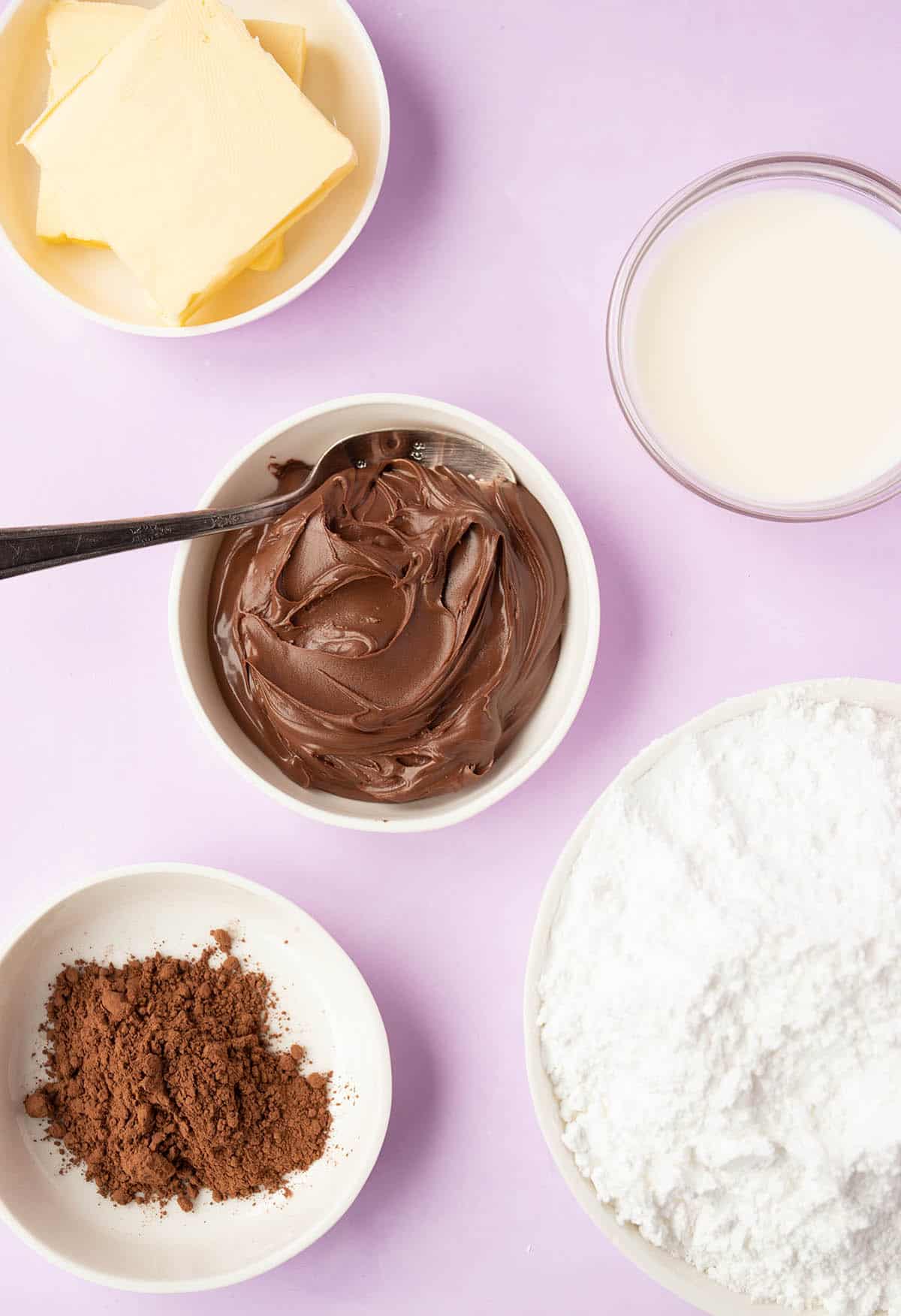 The ingredients needed to make Nutella Buttercream from scratch sitting on a purple background.