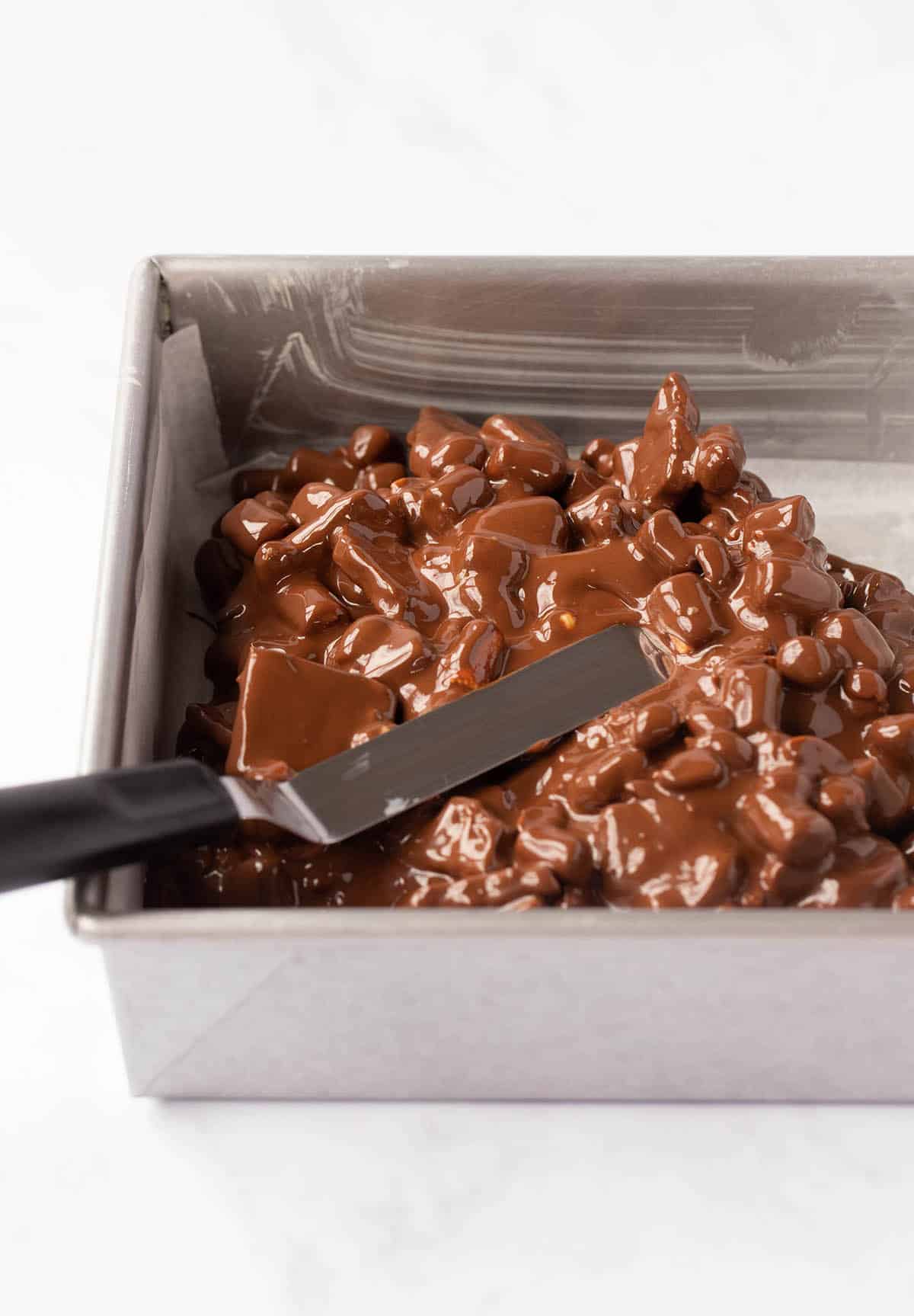 A baking pan filled with chocolate covered marshmallows, peanuts and Rolo. 