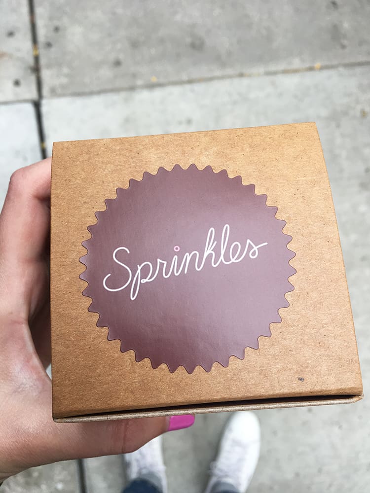 A hand holding a box from Sprinkles Cupcakes