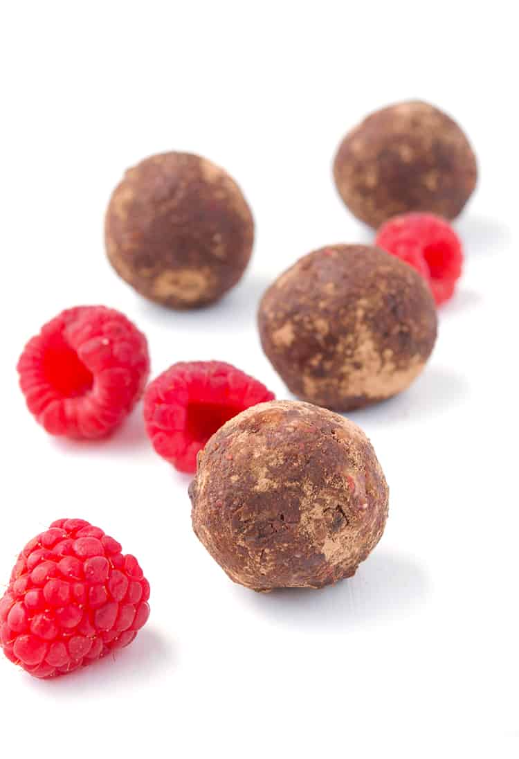 Chocolate Raspberry Bliss Balls in a white bowl with fresh raspberries