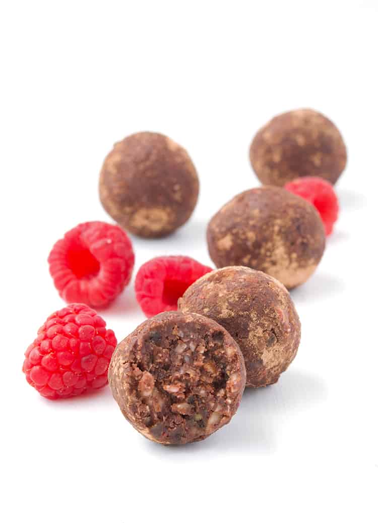 Chocolate Raspberry Bliss Balls in a white bowl with fresh raspberries