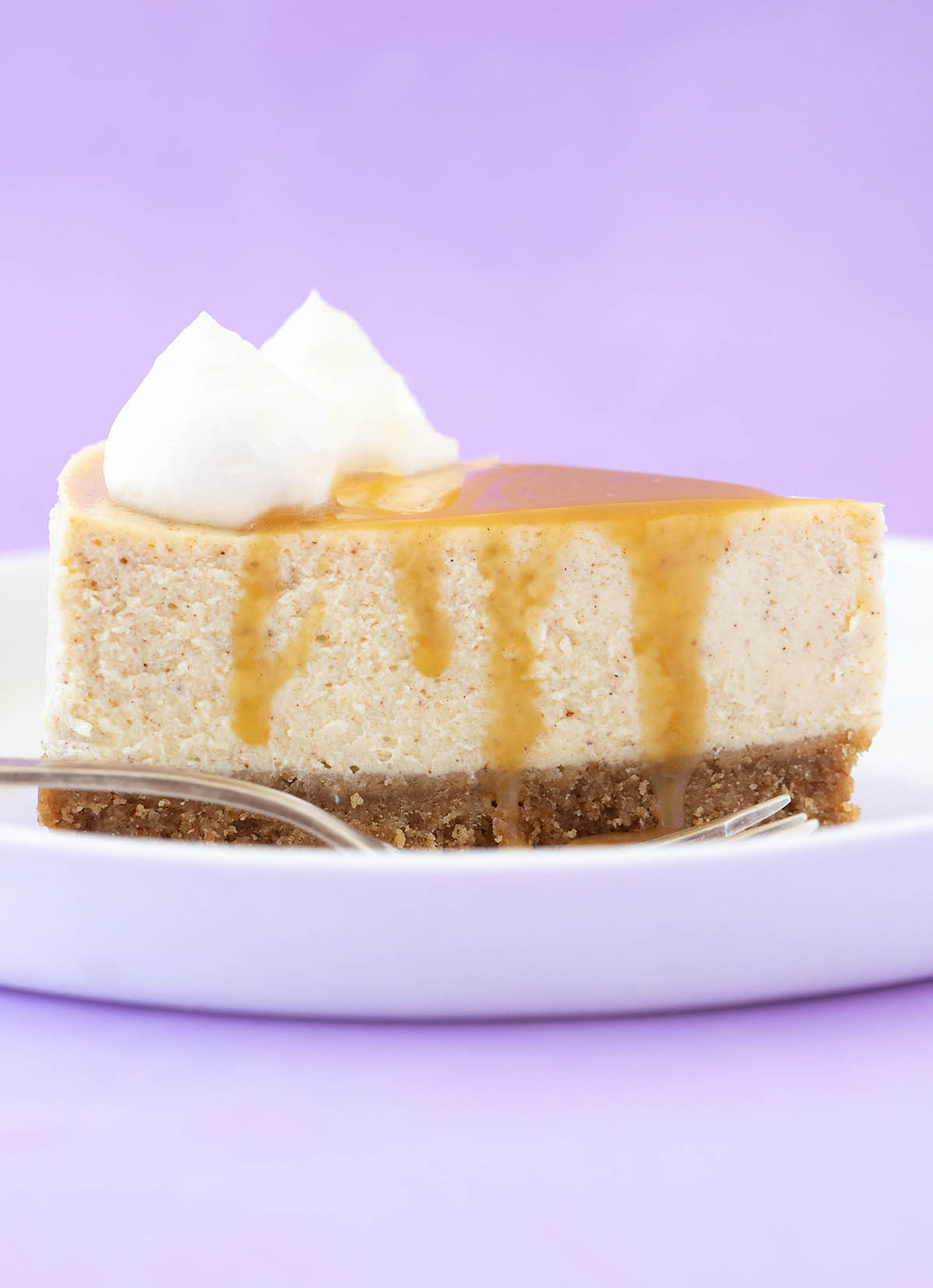Side shot of a slice of cheesecake covered in caramel on a white plate