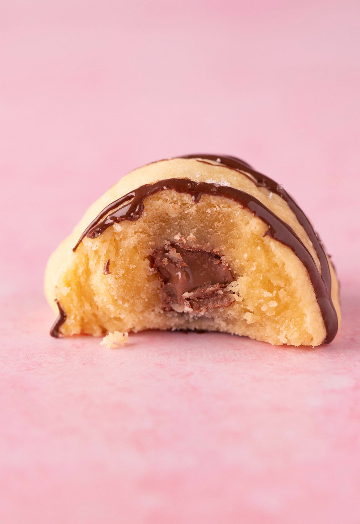 Buttery shortbread cookie filled with chocolate on a pink background.