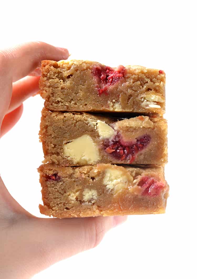 A hand holding a stack of White Chocolate and Raspberry Blondies