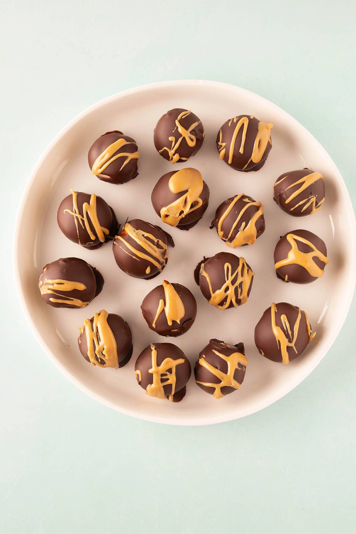 Lovely Peanut Butter Balls drizzled with peanut butter on a white plate. 