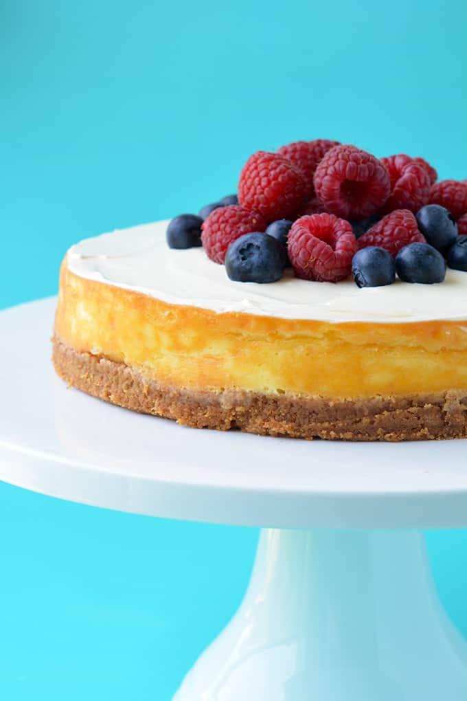 A baked Sour Cream Cheesecake on a white cake stand