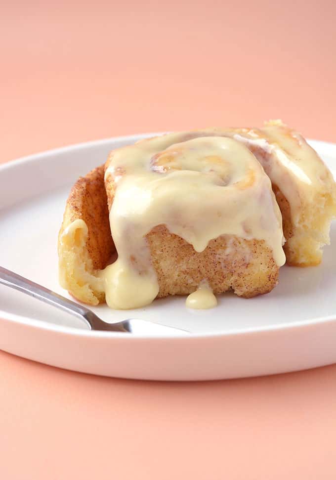 A cinnamon scroll dripping with cream cheese frosting on a plate