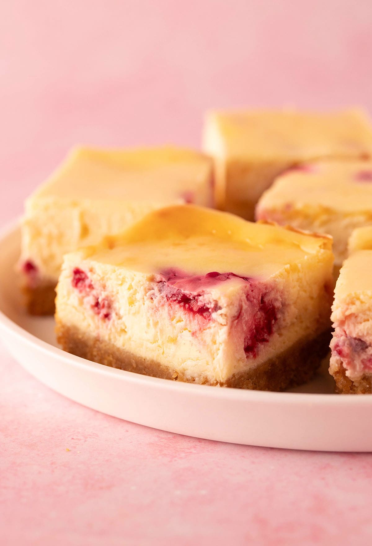 A plate of cheesecake bars filled with raspberries.