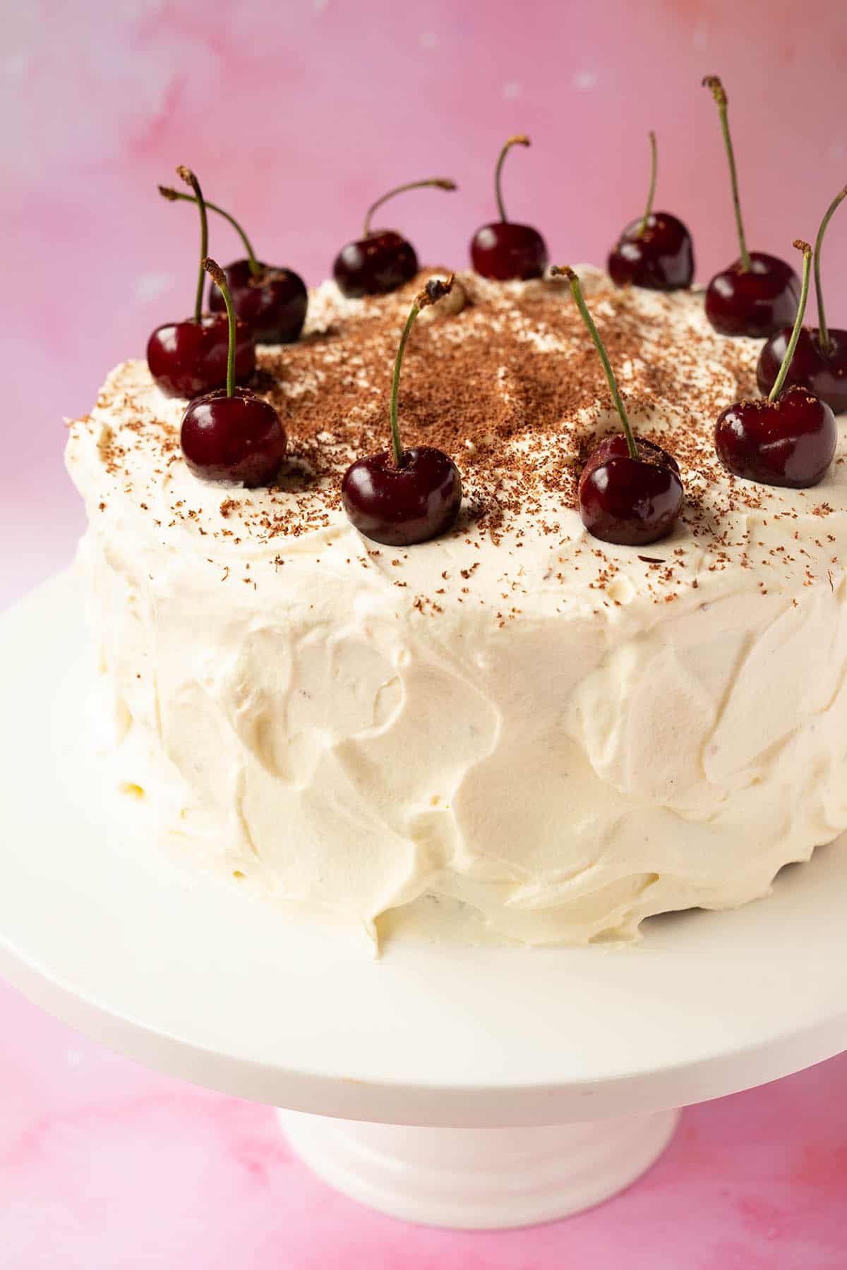 A beautiful Black Forest Cake decorated with fresh cherries on a white cake stand.