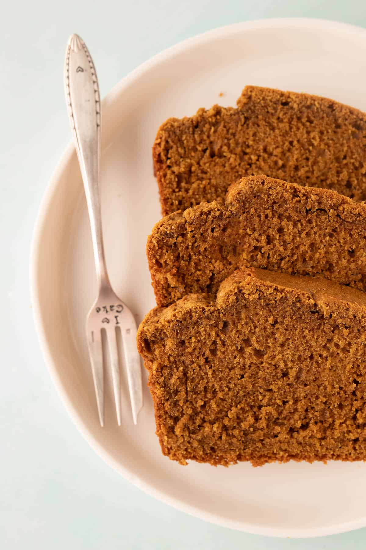 Slices of homemade Gingebread Load on a white plate with a decorative fork.