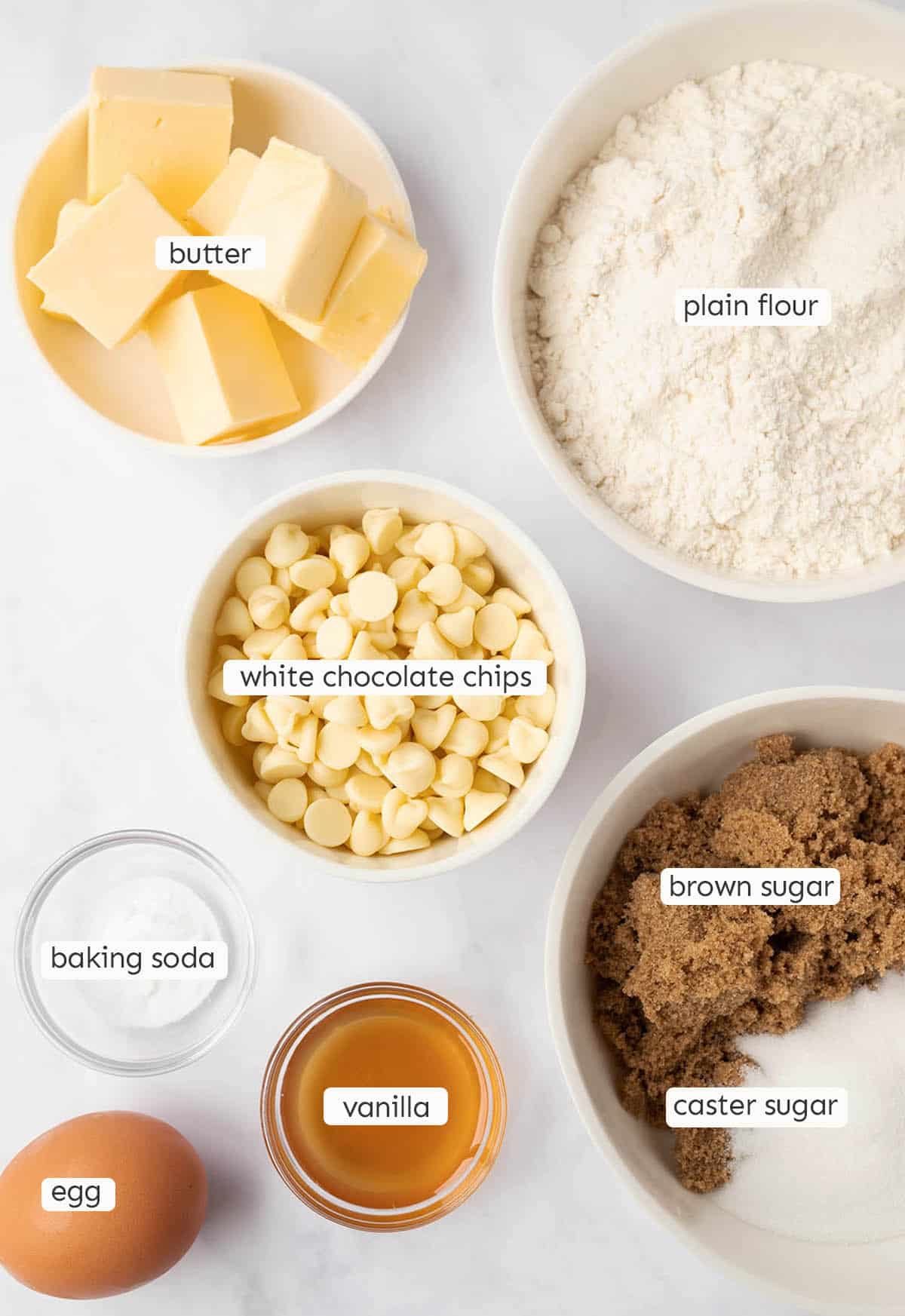 All the ingredients needed to make white chocolate chip cookies from scratch on a marble backdrop.