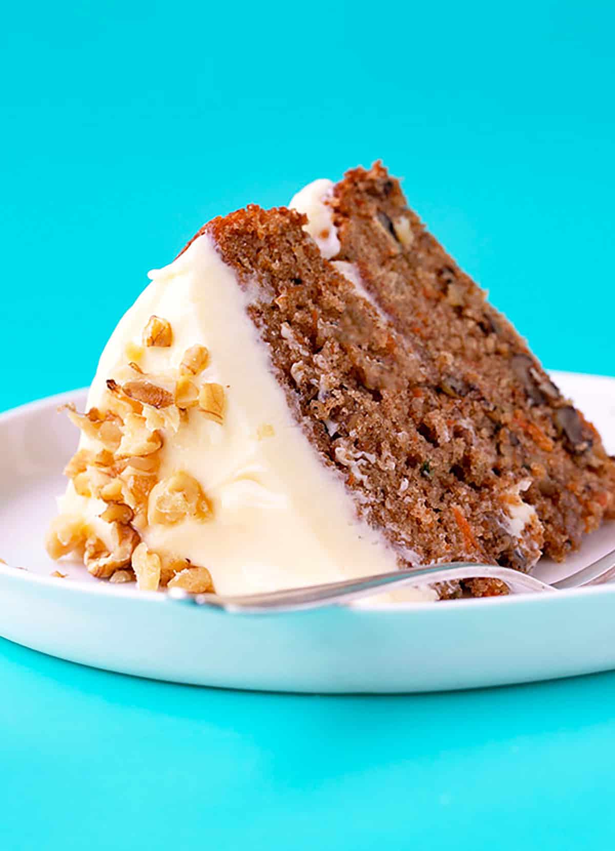A slice of carrot cake with cream cheese frosting on a white plate. 