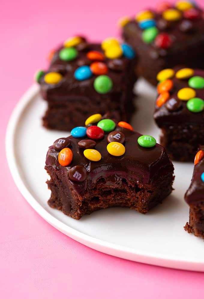 A plate of M&M Chocolate Frosted Brownies with a bite taken out of it