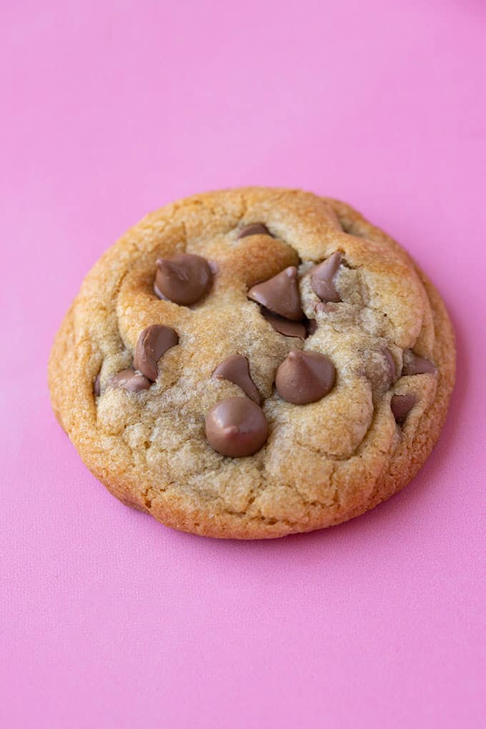 A close up of a chocolate chip cookie on a pink background