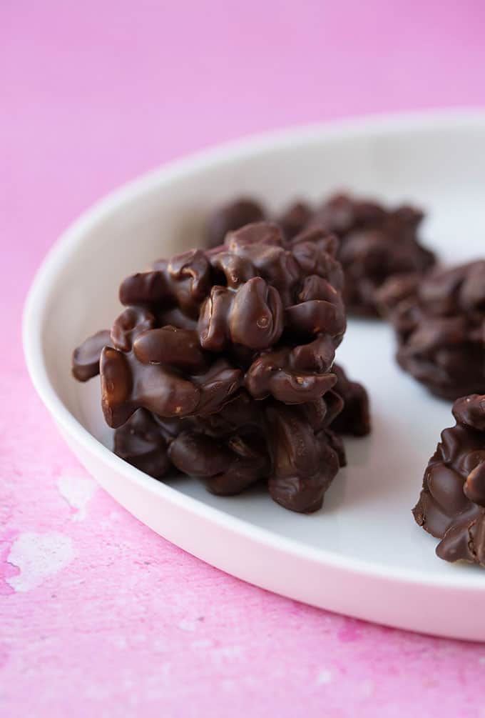 A stack of homemade Chocolate Peanut Clusters on a white plate