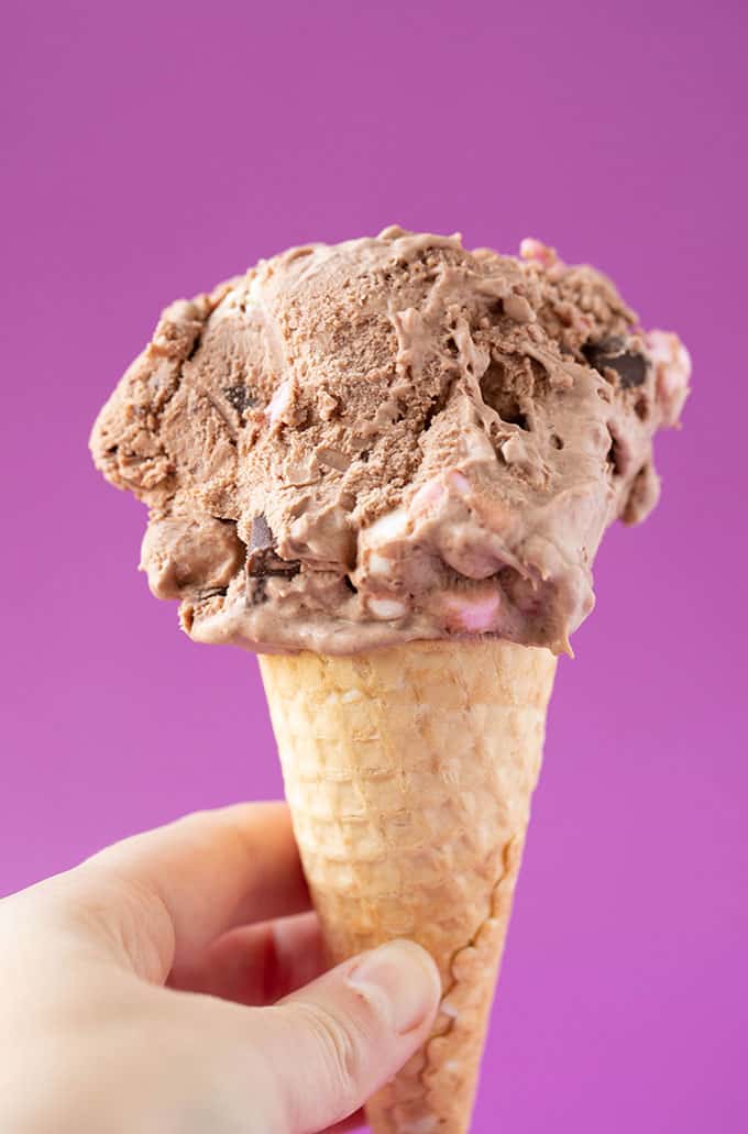 A hand holding an ice cream cone filled with rocky road ice cream