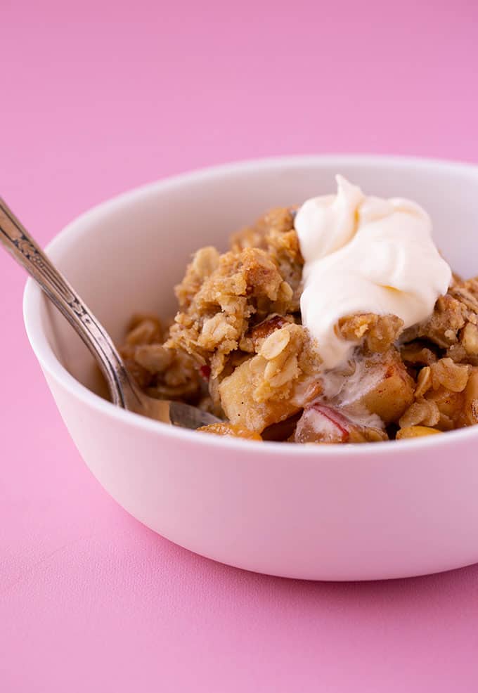 A white bowl of Apple Crumble on a pink background