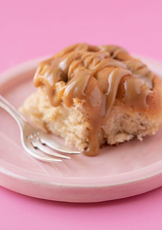A caramel apple bun drizzled with caramel on a pink plate