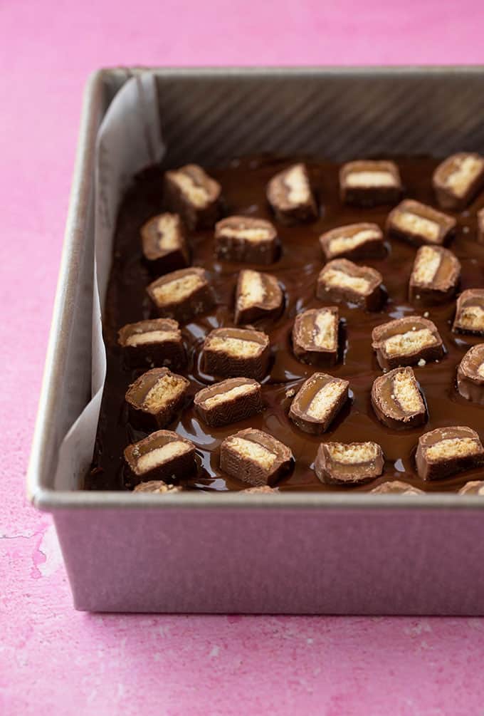 A chocolate slice covered in Twix Bars still in baking tin