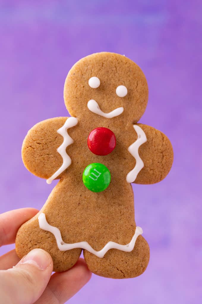 A hand holding a Gingerbread Cookie on a purple background
