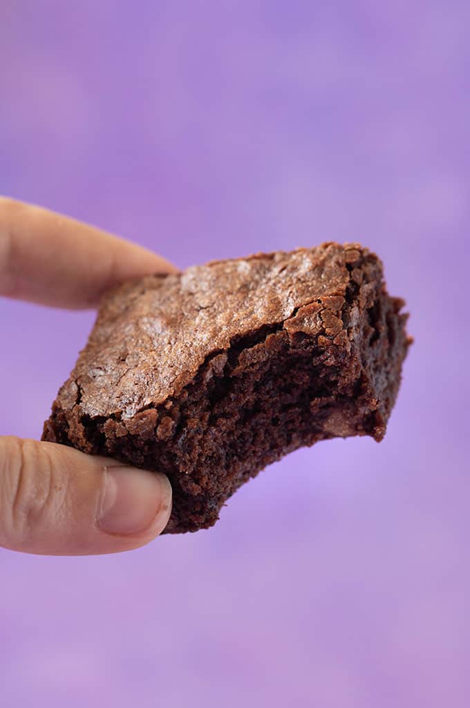 A hand holding a Coconut Oil Brownie with a bite taken out of it