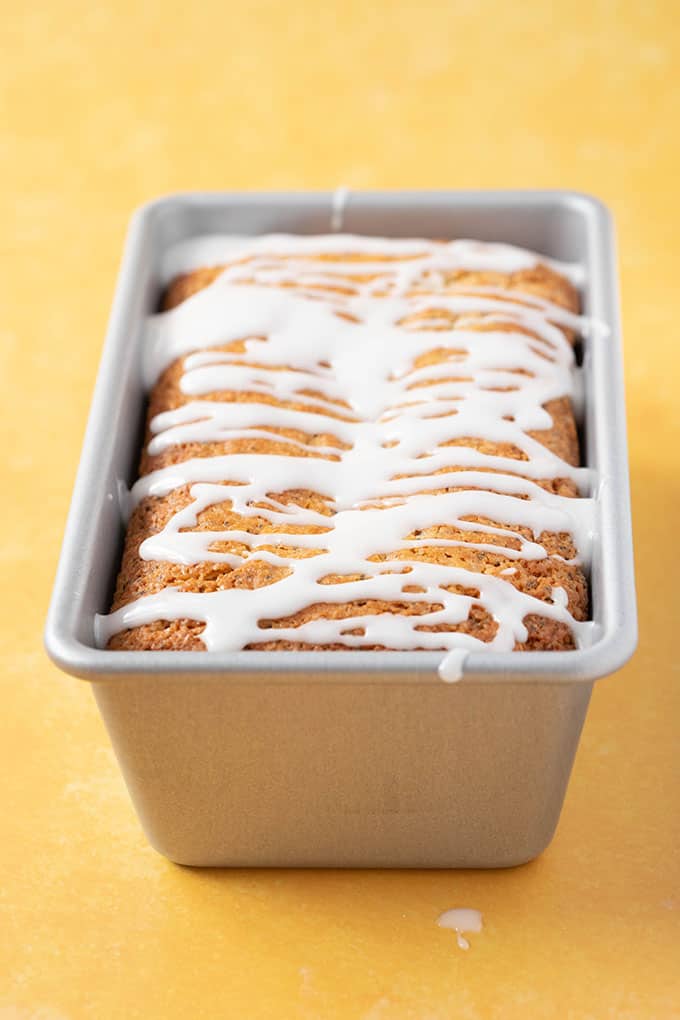 A homemade Lemon Poppy Seed Loaf sitting in it's baking pan on a yellow background