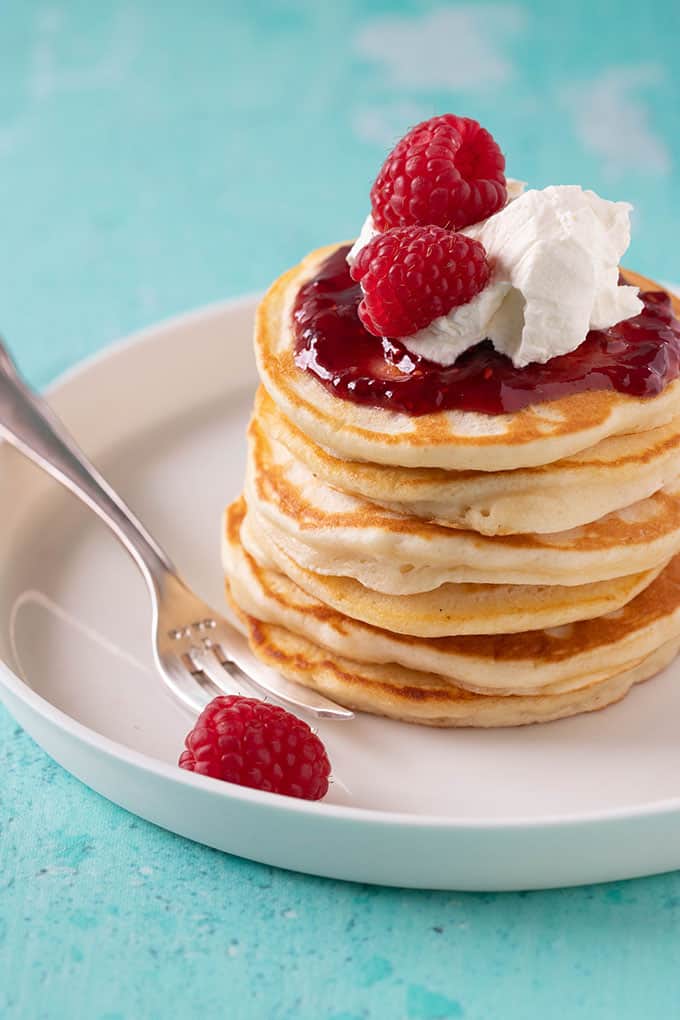 A plate of Pikelets and fresh raspberries on a blue background