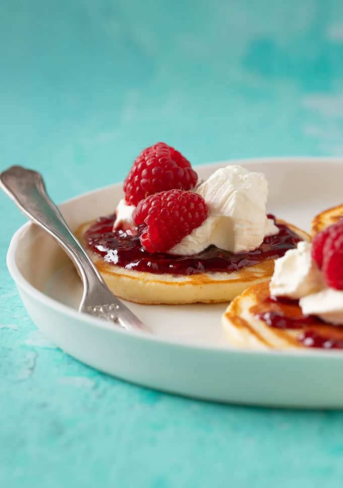 A plate of homemade mini pancakes topped with jam and cream
