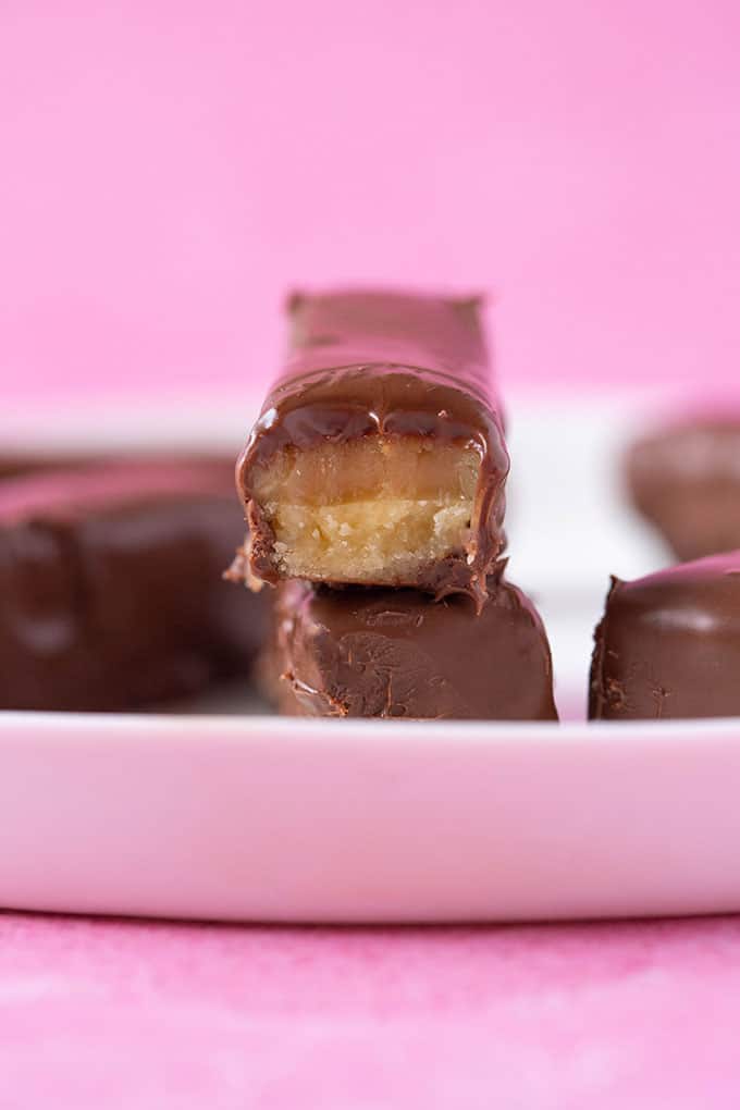 Close up view of Homemade Twix Bars with chewy caramel on a pink background