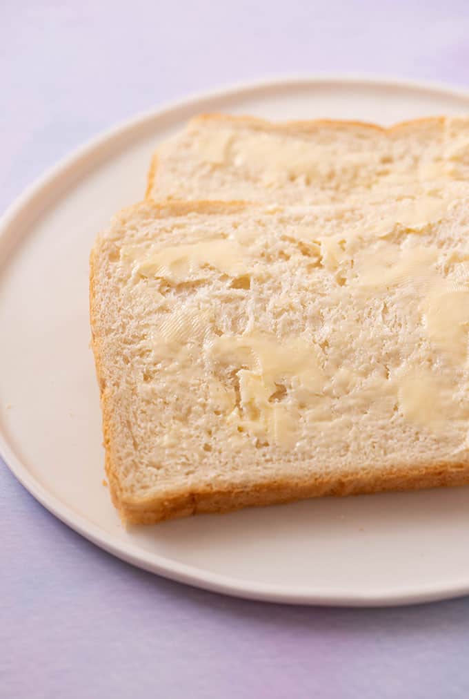 Two pieces of buttered white bread on a white plate
