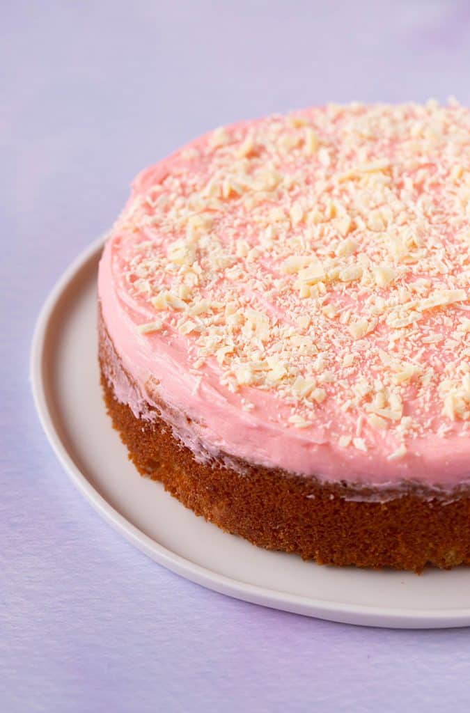 A homemade Butter Cake with pink buttercream on a purple background
