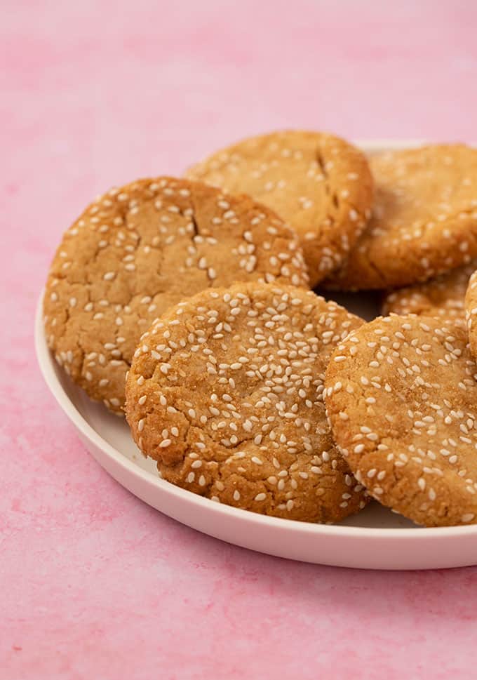 A plate of Tahini Cookies rolled in sesame seeds on a pink background