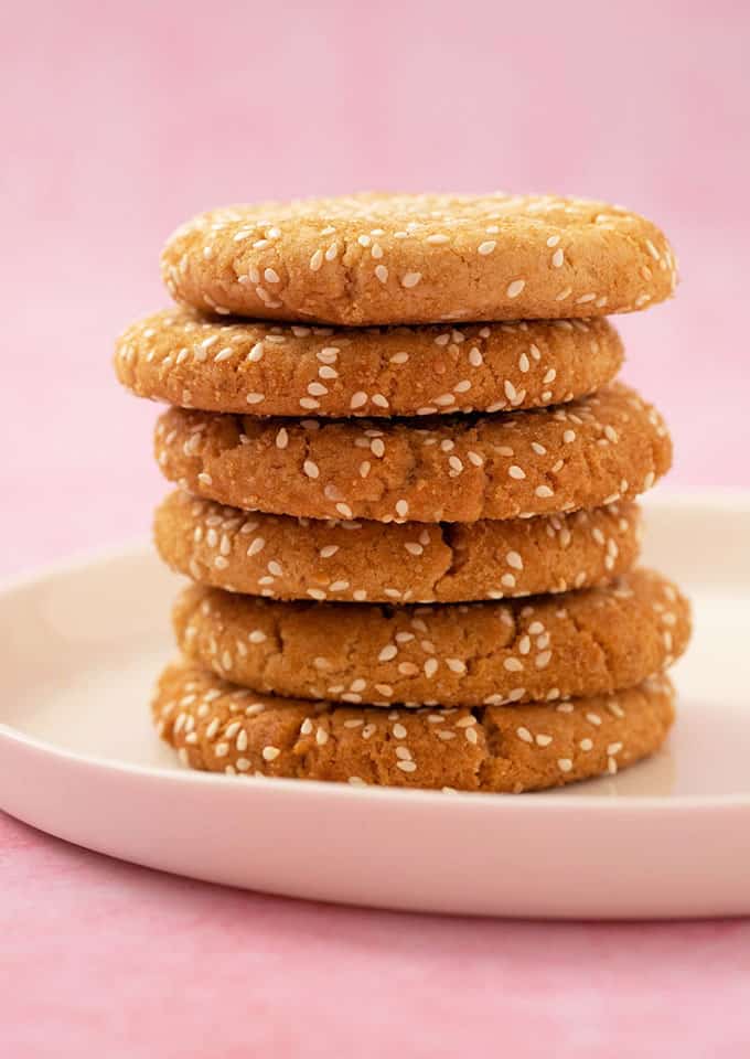 A tall stack of homemade Tahini Cookies on a white plate with a pink background