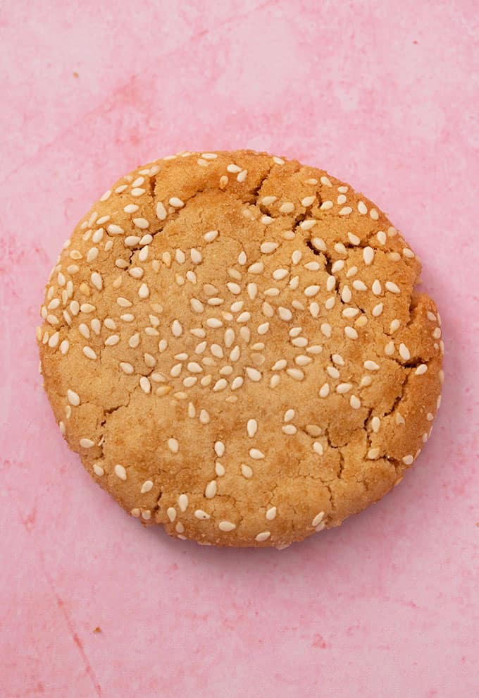 Close up of a single Tahini Cookie rolled in sesame seeds on a pink background