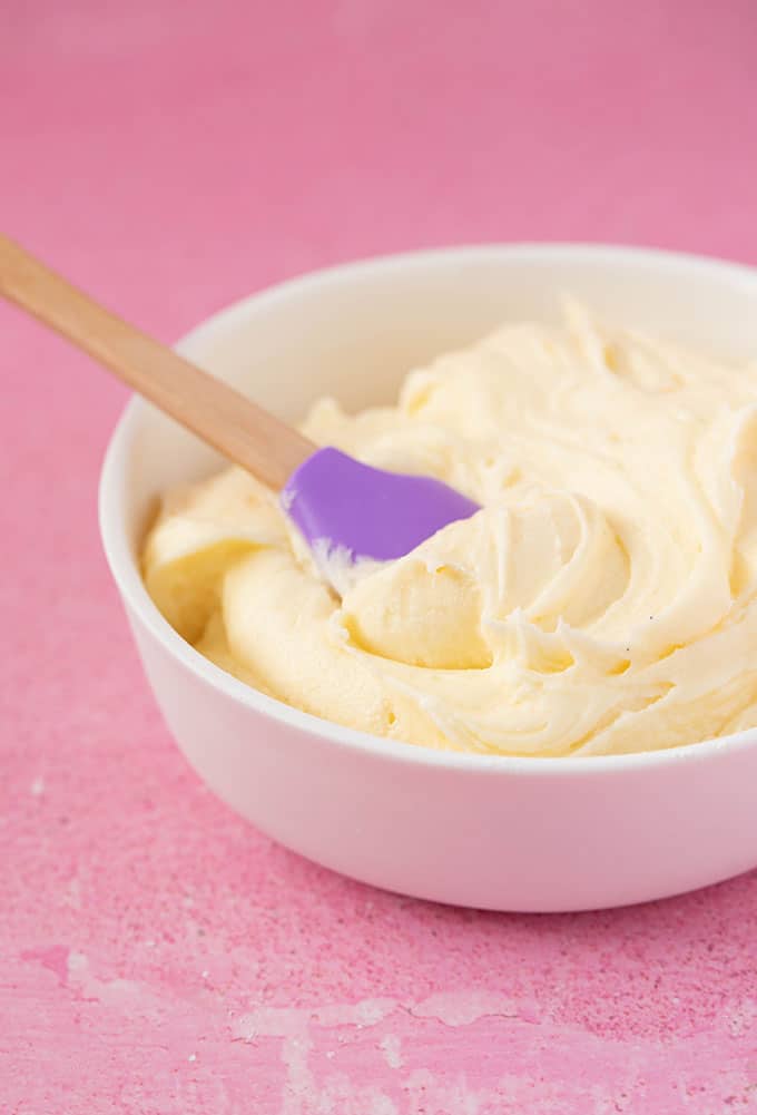 A bowl of homemade vanilla buttercream on a pink background