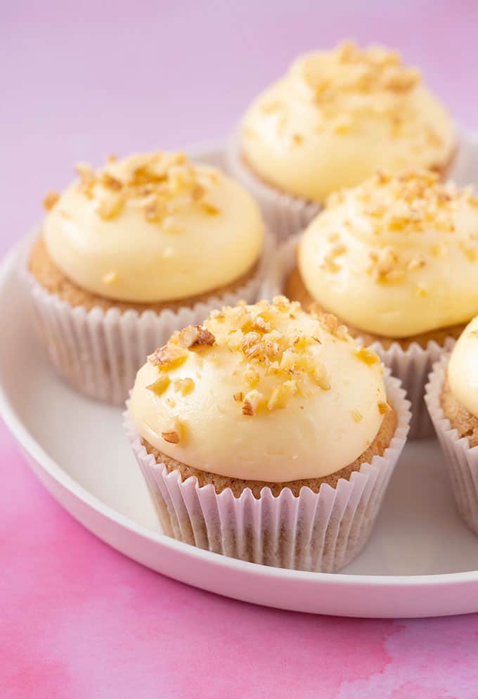 A white plate of Banana Cupcakes topped with cream cheese frosting