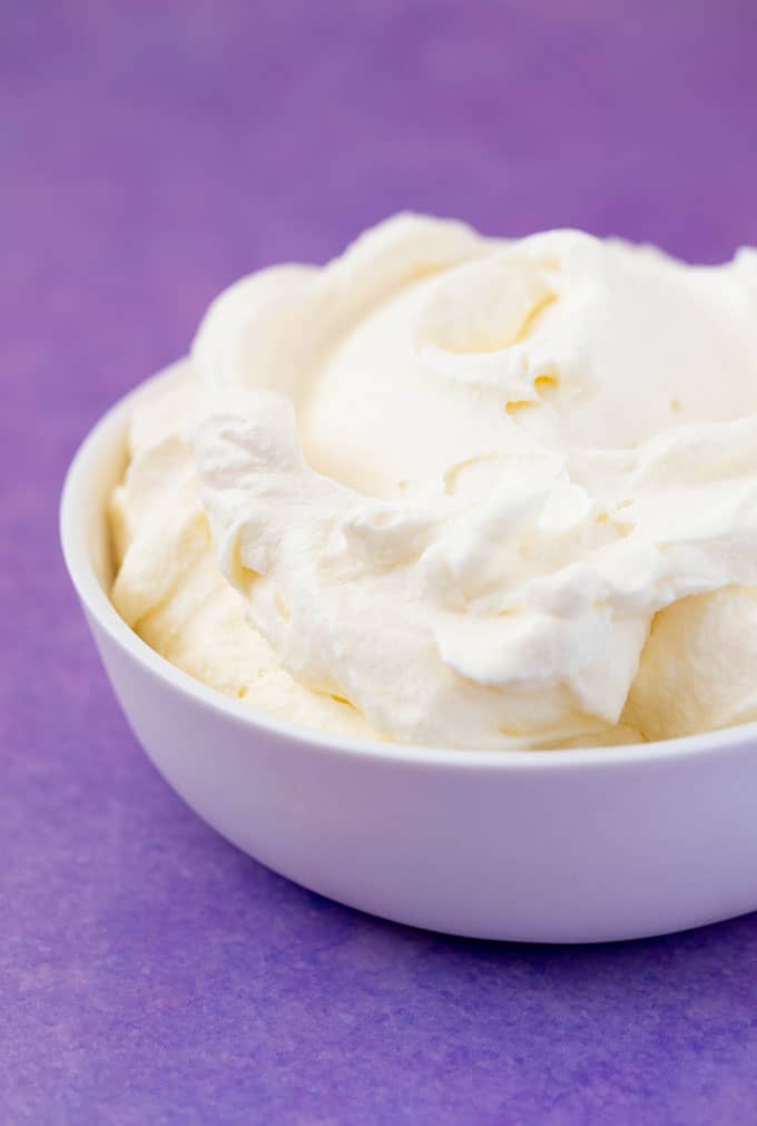 A bowl of homemade whipped cream on a purple background