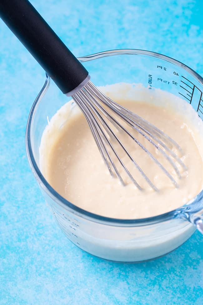 A glass jug of homemade pancake batter with a whisk in it