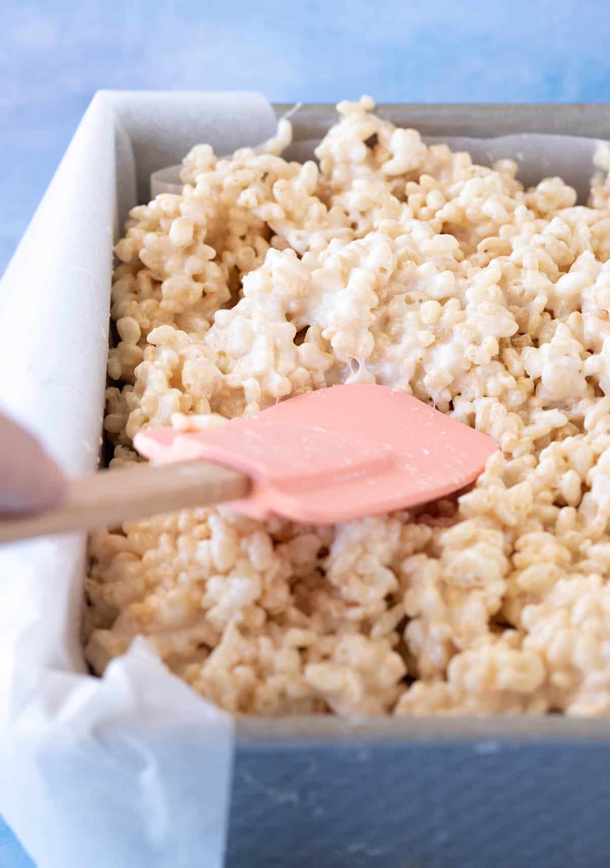 A spatula pressing down marshmallow Rice Krispie Treats into a pan. 