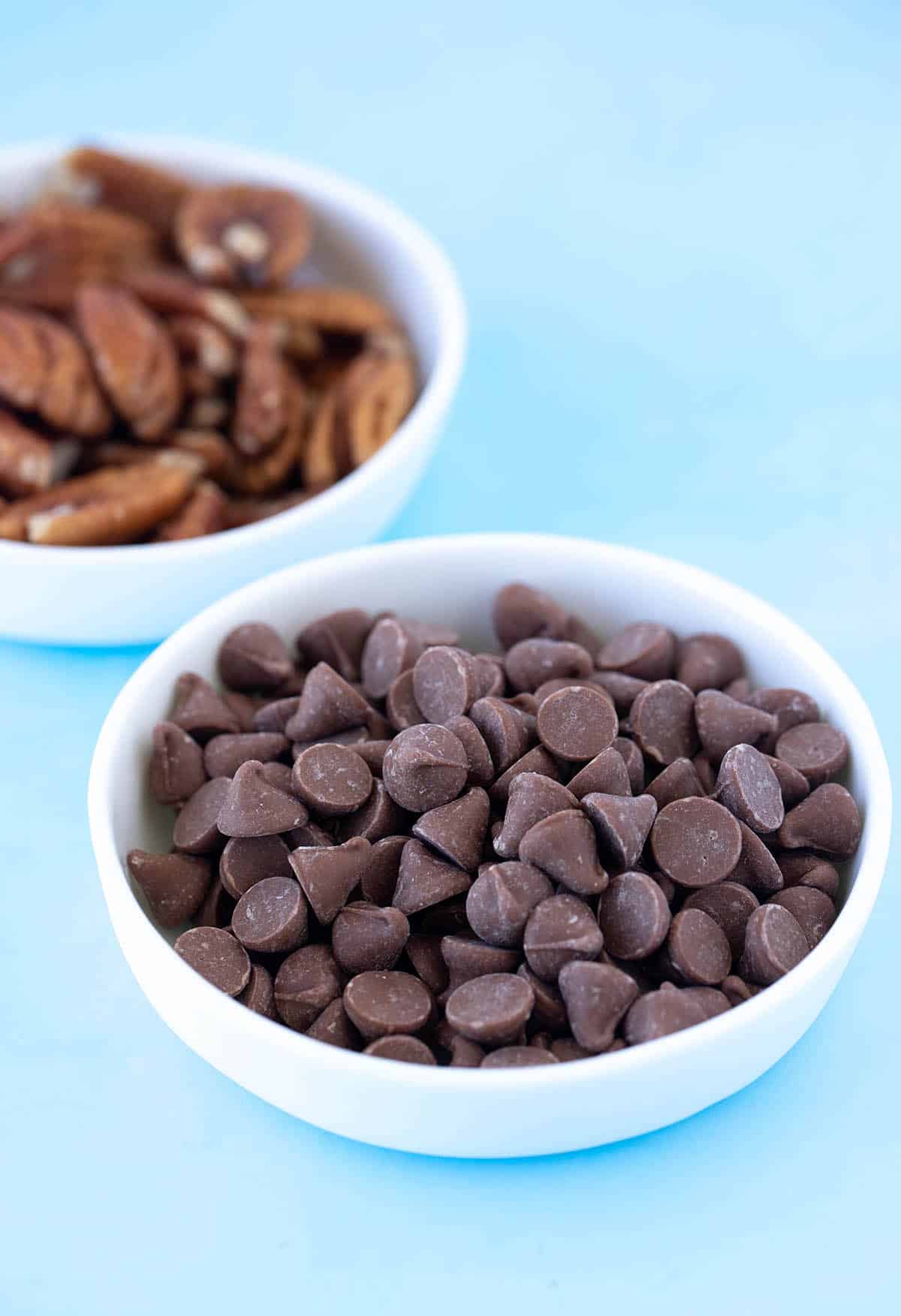 A bowl of chocolate chips and a bowl of pecans