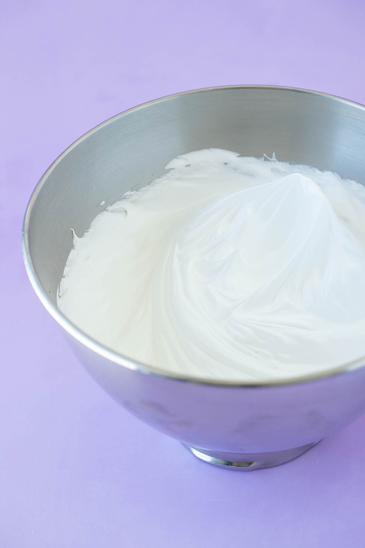 A metal mixing bowl filled with egg whites that have been whipped to stiff peaks. 