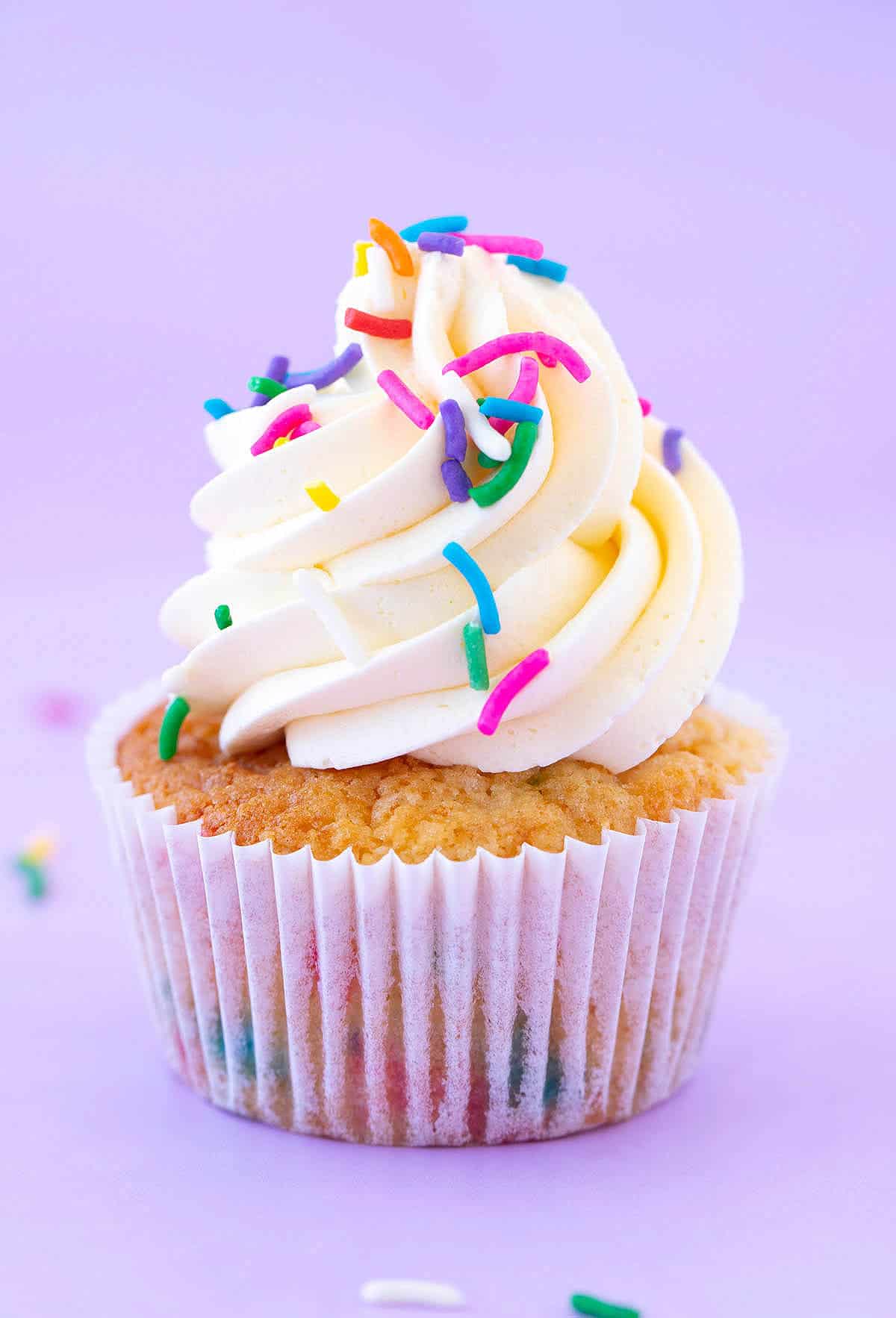 A beautiful cupcakes topped with swirls of frosting on a purple background.