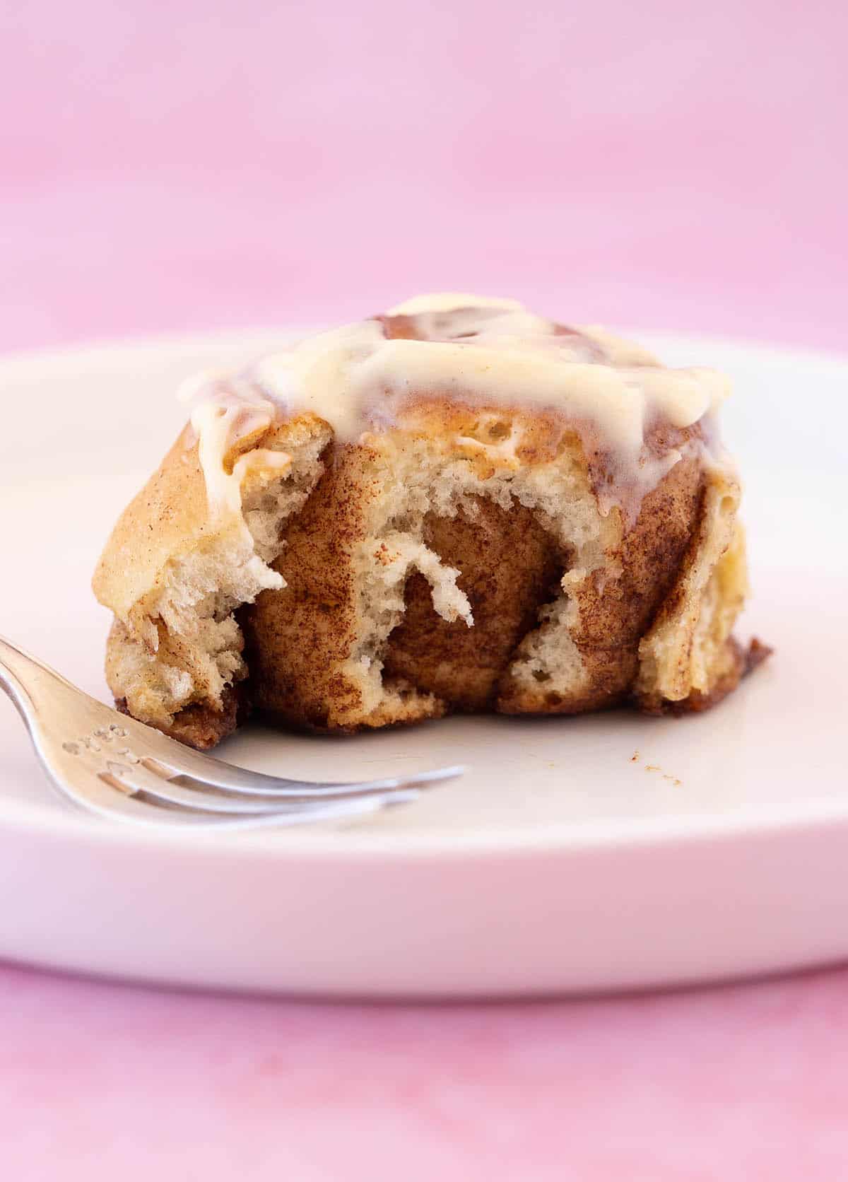Close up of a homemade cinnamon bun with a bite taken out of it revealing the layers.