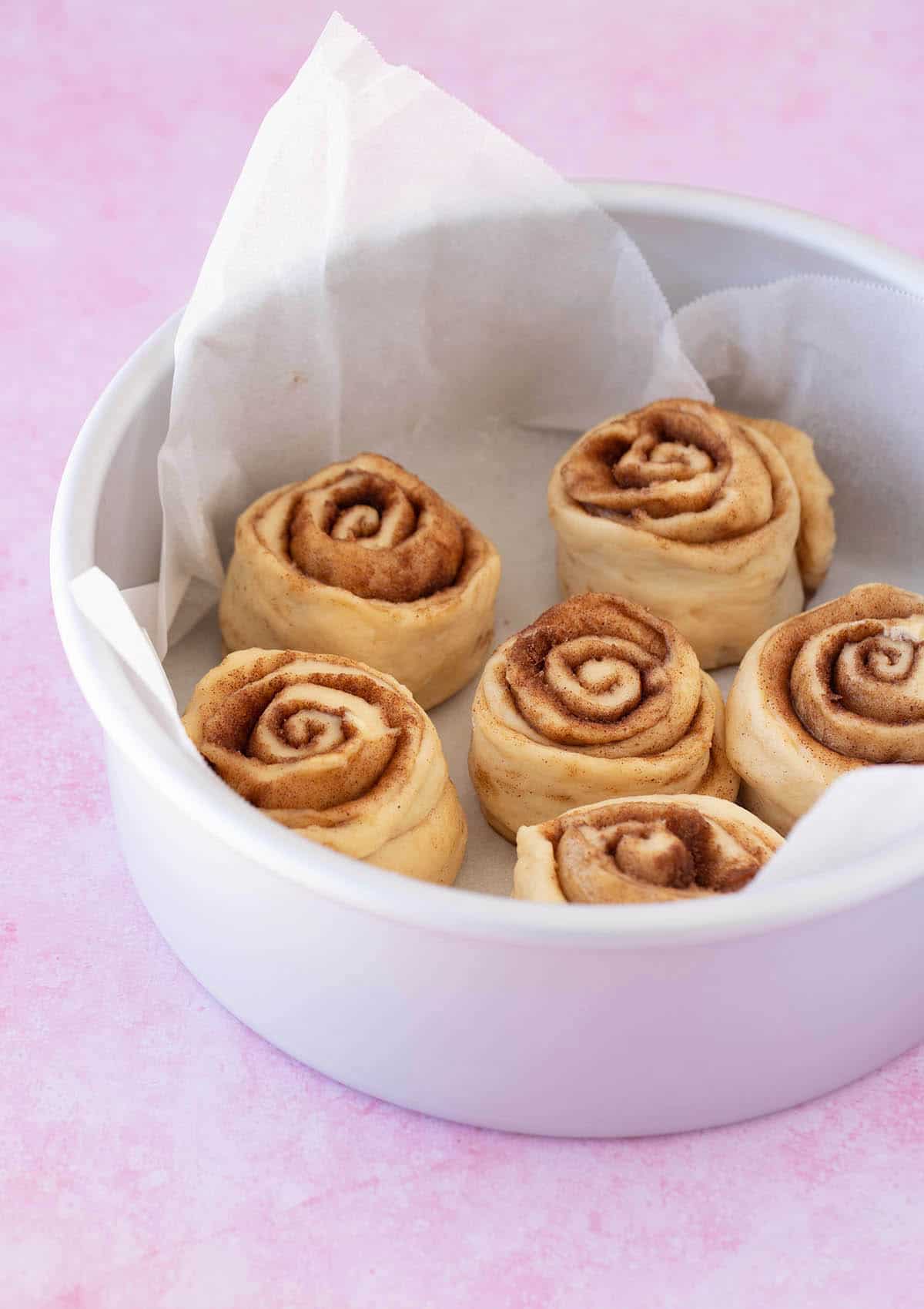 Six cinnamon rolls sitting in a cake pan ready to be baked