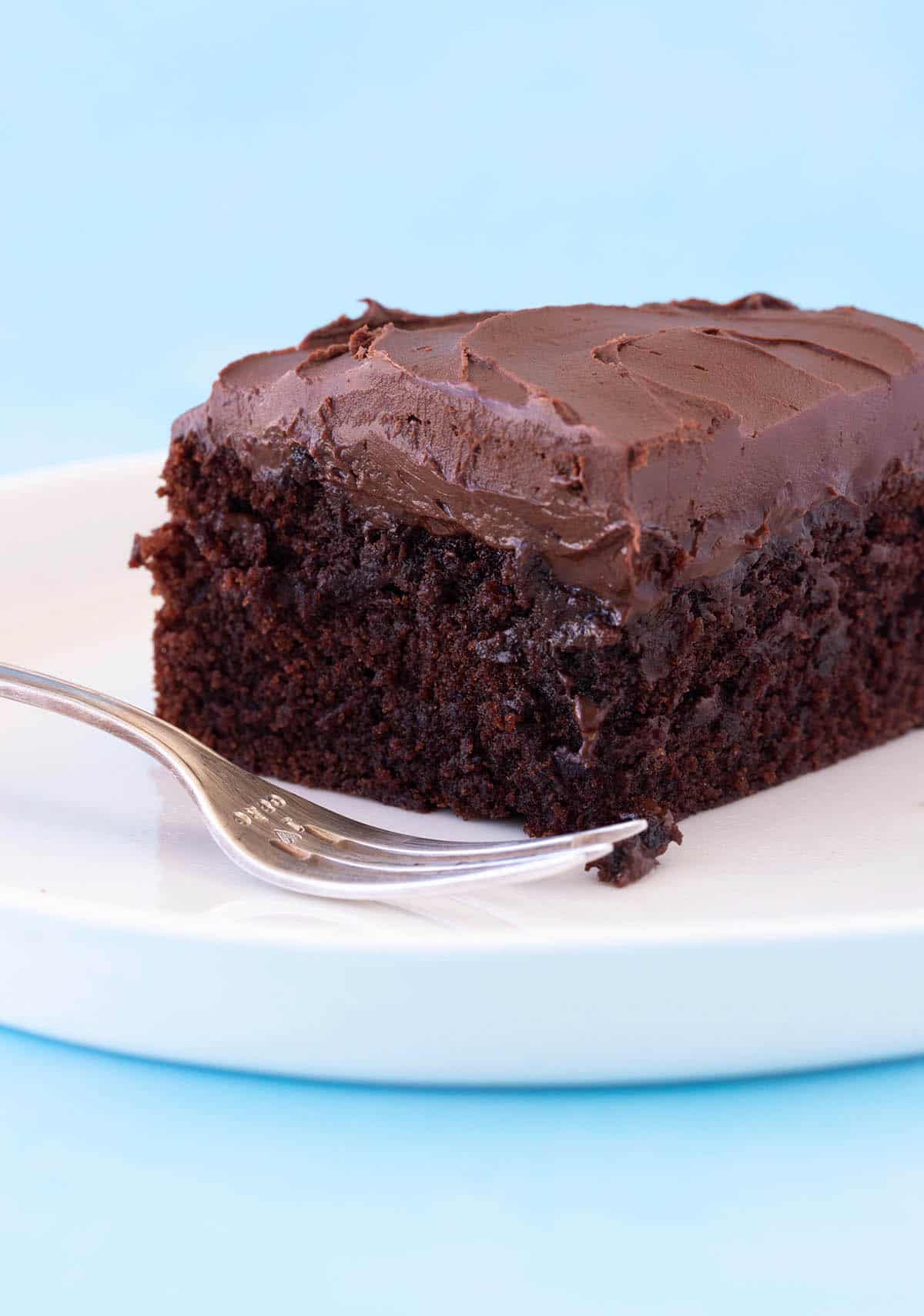 A slice of Chocolate Cake on a white plate with a serving fork