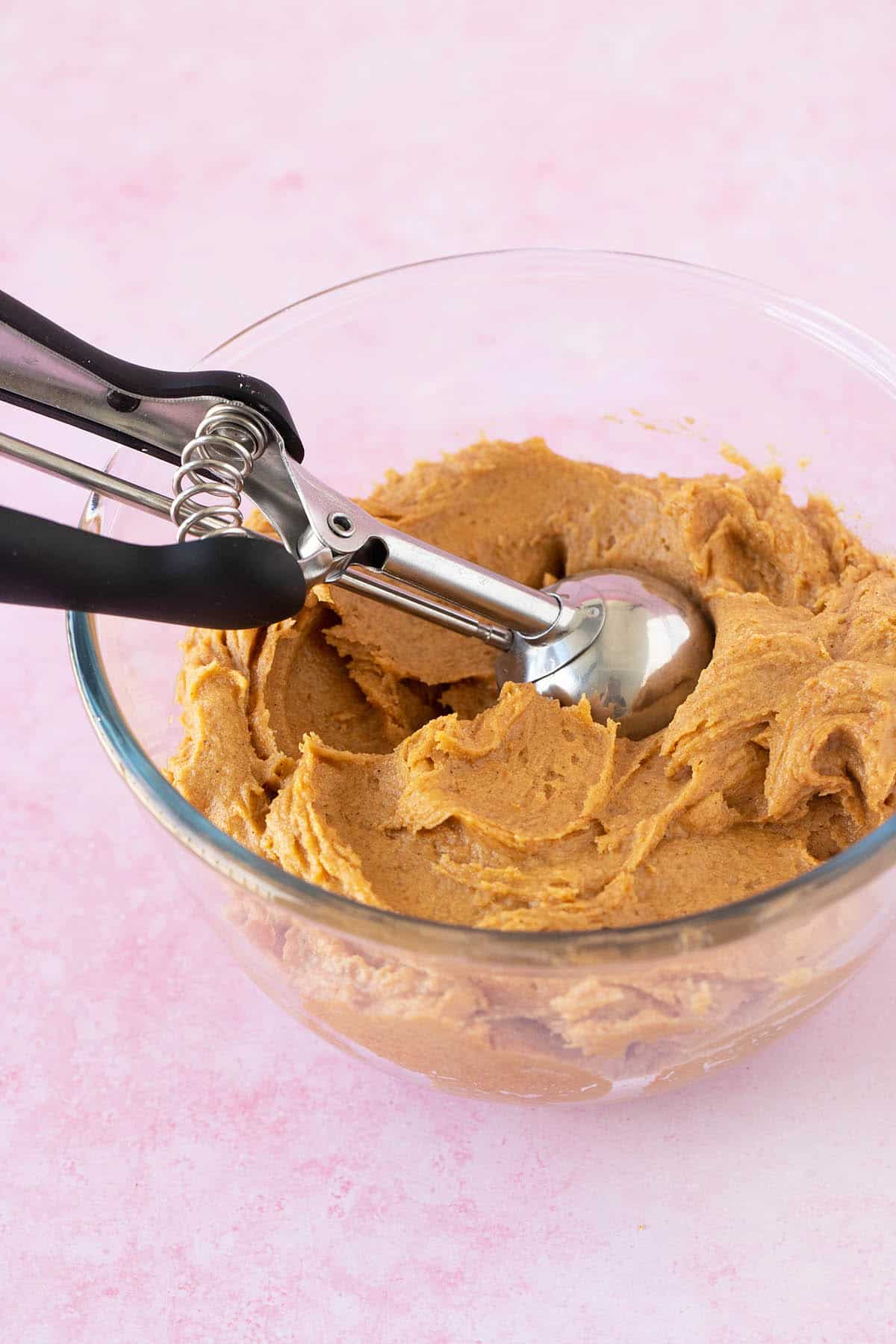 A glass bowl filled with pumpkin cookie batter and a cookie scoop.