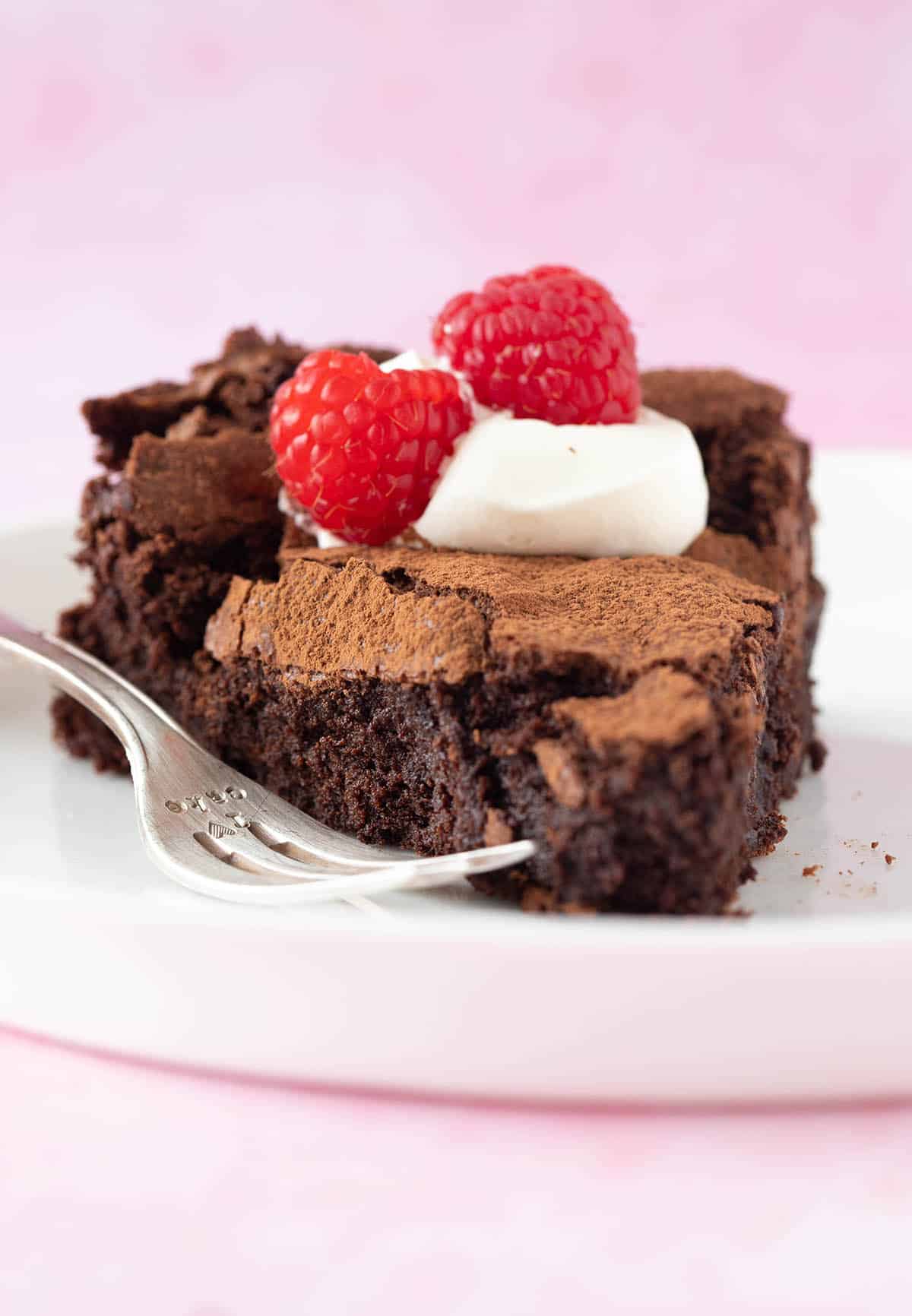 Close up of a fudgy slice of flourless chocolate cake decorated with cream and berries.